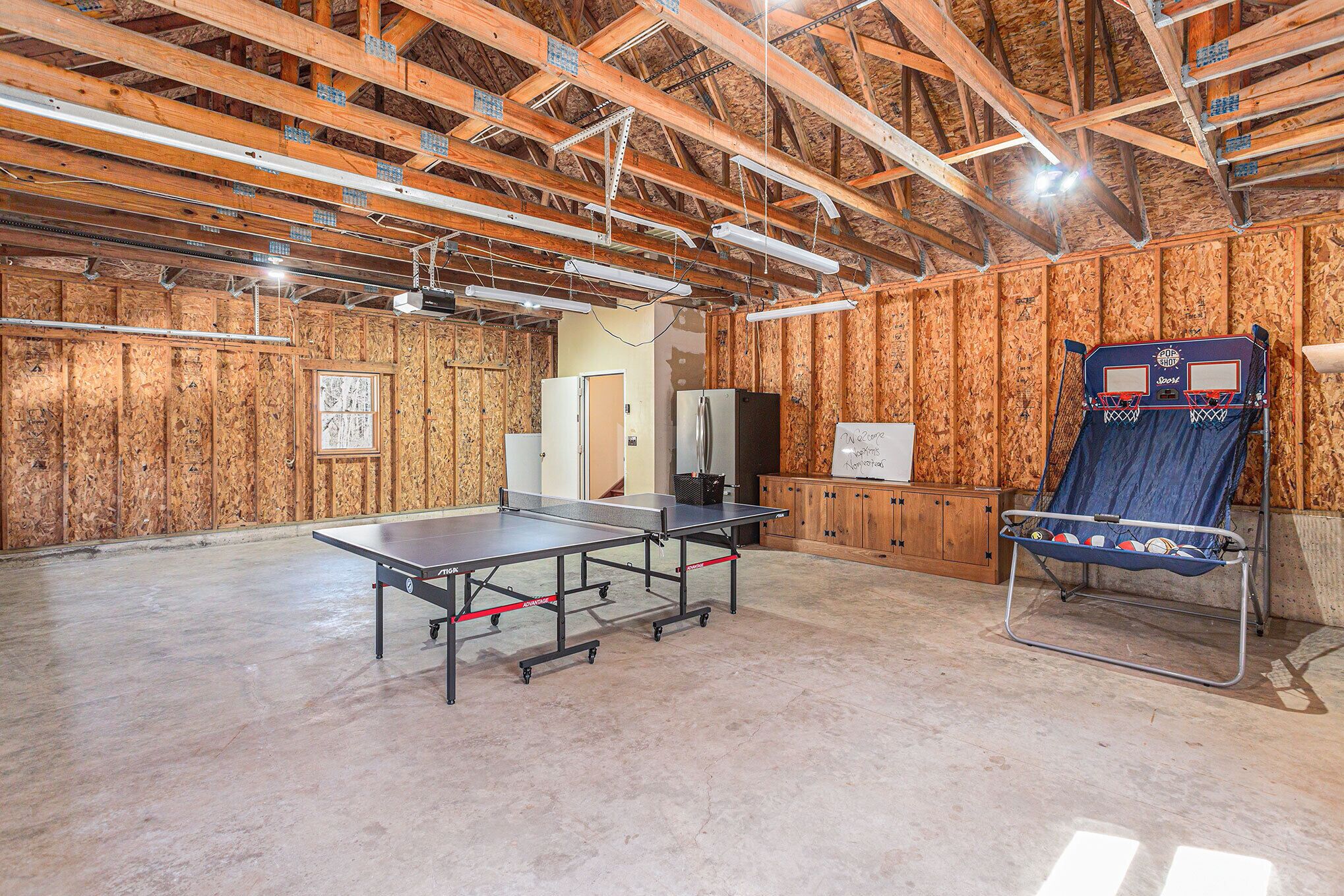 A spacious room with a ping pong table, a basketball hoop, and a blue chair.