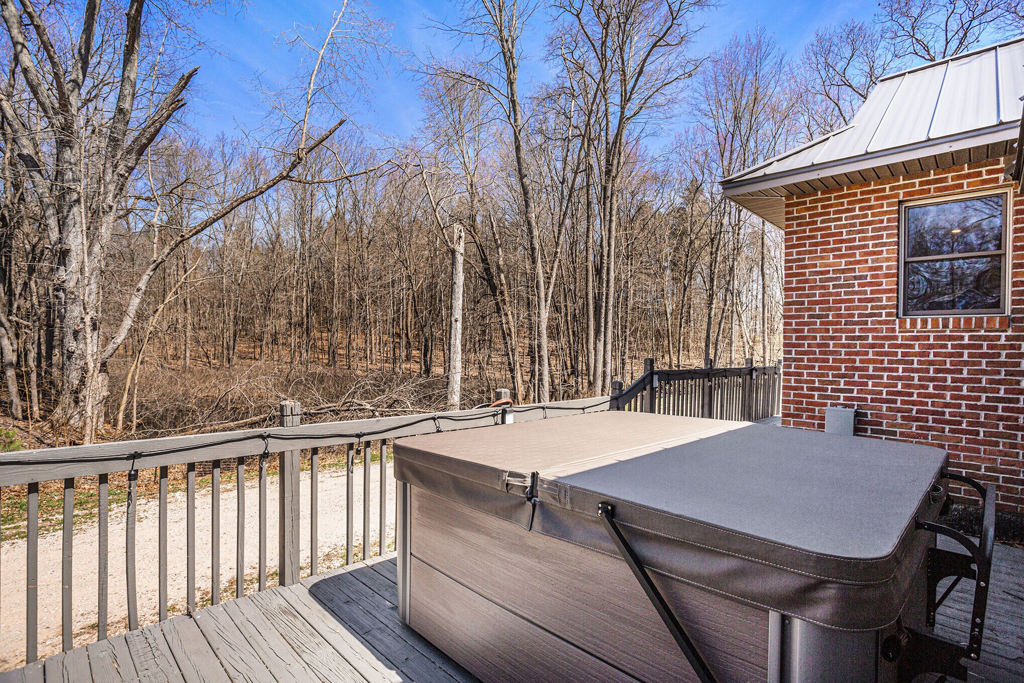 Une terrasse avec un jacuzzi, un bâtiment en briques et une zone boisée en arrière-plan.