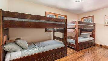 A room with two bunk beds, wooden flooring, and framed artwork on the walls.