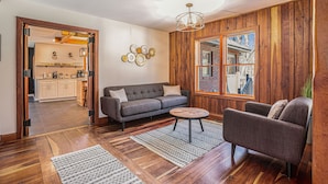 A living room with a sofa, armchair, coffee table, and a view of a kitchen and dining area through an open doorway. - Private 40-Acre Retreat | Hot Tub, Trails, Games & Fire Pit (Hopkins)