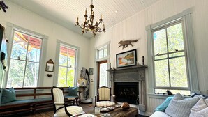 A cozy living room with a fireplace, wooden furniture, and large windows offering a view of the outdoors.