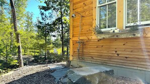 Una cabaña de madera con un banco de piedra y una ventana con vista al bosque.