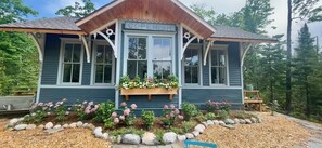 Un piccolo edificio a due piani con un portico, con la scritta "COPENISH", circondato da un giardino con diverse piante e fiori.