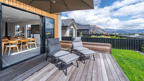 Eine Terrasse mit zwei grauen Liegestühlen, einem Holztisch und einem Sonnenschirm.