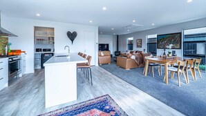 Eine moderne Küche mit Kochinsel, ein Essbereich mit Holztisch und Stühlen sowie eine Wohnbereich mit Sofa und Fernseher.