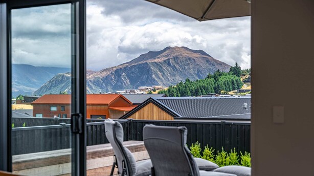Ein Balkon mit zwei Stühlen und einem Tisch, mit Blick auf einen Berg und eine Stadt.