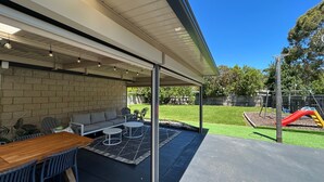 An outdoor patio area with a brick wall, a wooden table, and two white chairs. - Sandy Retreat on Royal Inverloch (Inverloch)