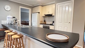 A kitchen with a black countertop, white cabinets, a refrigerator, and a clock on the wall. - Sandy Retreat on Royal Inverloch (Inverloch)