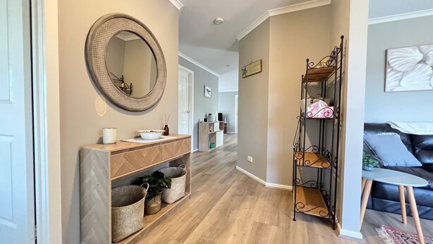 A hallway with a wooden floor, a round mirror, a wooden console table with baskets, and a metal shelf unit. - Sandy Retreat on Royal Inverloch (Inverloch)