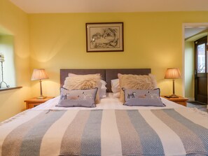 A double bed with striped bedding, two pillows with dog prints, a framed owl artwork above the bed, and two bedside lamps on wooden nightstands. - Bradley Stables (Minehead)