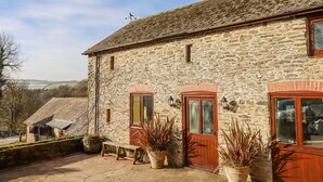 A stone building with a red door and windows, a bench, and potted plants. - Bradley Stables (Minehead)