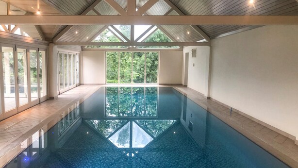 An indoor swimming pool with a clear view of the surrounding greenery through large windows. - Bradley Stables (Minehead)