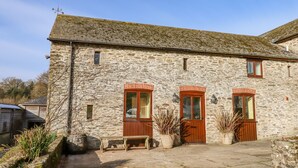 A stone building with two wooden doors and windows, a bench, and potted plants. - Bradley Stables (Minehead)