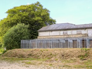 A rustic wooden building with a stone foundation, surrounded by a metal fence. - Bradley Stables (Minehead)