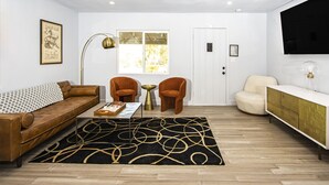 A modern living room with a brown leather sofa, two orange armchairs, a black and gold rug, a white cabinet, and a large window. - Experience the magic of Joshua Tree. Your cozy bungalow awaits. (Twentynine Palms)