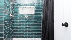 A bathroom with teal mosaic tiles, a shower with a handheld showerhead, and a black shower curtain. - Experience the magic of Joshua Tree. Your cozy bungalow awaits. (Twentynine Palms)