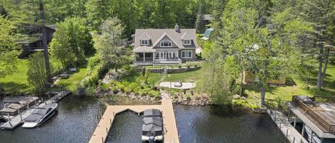 A large house with a dock and boats, surrounded by dense trees.
