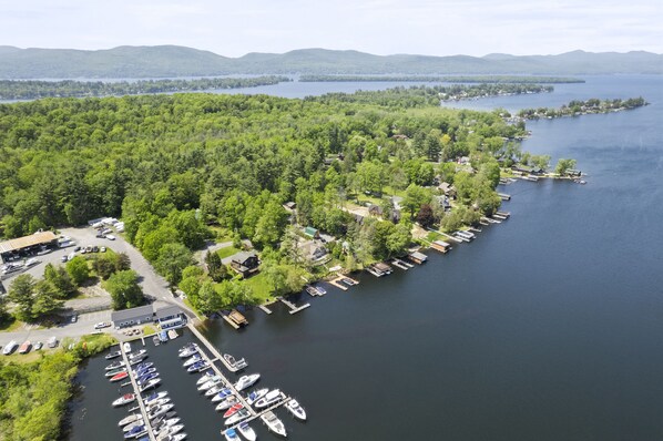 An aerial view of a lakeside property with a marina, docked boats, and a forested area.
