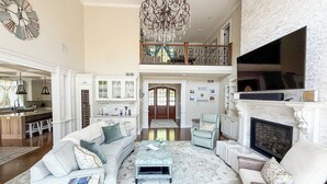 A spacious living room with a high ceiling, a chandelier, a fireplace, and a large TV. - Paradise Bay (Queensbury)