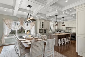 A spacious dining area with a long wooden table set for a meal, surrounded by white chairs.