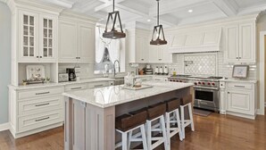 A spacious kitchen with white cabinetry, a large island with bar stools, pendant lighting, and a built-in oven. - Paradise Bay (Queensbury)