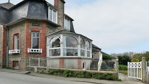 Un immeuble d’angle avec une façade en pierre, une grande baie vitrée et une clôture blanche.