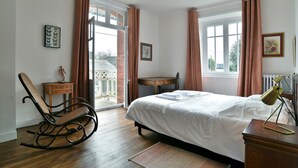 Une chambre à coucher avec un lit, un fauteuil à bascule, une petite table et une fenêtre avec des rideaux.