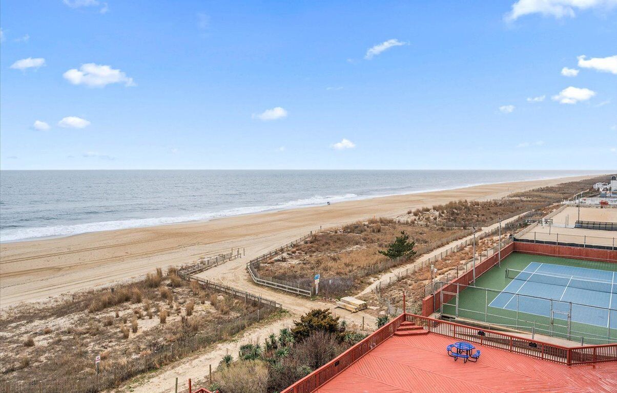 A beach view with a tennis court and a red-roofed building.
