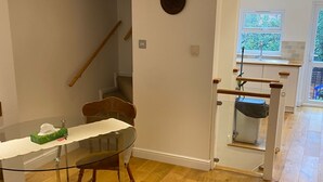 Een eetgedeelte met een glazen tafel en houten stoelen, een houten trap en uitzicht op het groen door een raam.