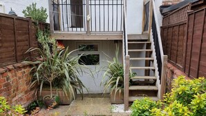 Een wooneiland met een gebouw van twee verdiepingen, een houten trap, een omheinde tuin en een klein pad.