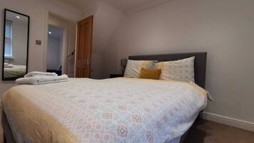 A bedroom with a large bed, a mirror, a door, and a nightstand.