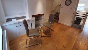 Een moderne keuken met een glazen eettafel, houten vloeren en een trap die naar een hoger niveau leidt.