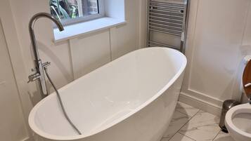 A bathroom with a freestanding bathtub, a window with a view of greenery, and a towel rack.