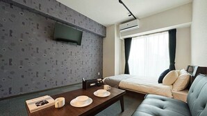 Une chambre d’hôtel comprenant un lit, un canapé, un téléviseur fixé au mur, une table à manger avec des assiettes et des tasses, et un appareil de climatisation.