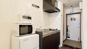 Une cuisine compacte équipée d’un four à micro-ondes, d’une cuisinière et d’un évier. On y trouve une porte avec un panneau indiquant la sortie et une petite fenêtre.