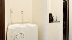 A laundry room with a white washing machine, a shelf with a coffee maker, and a door leading to another room. - Nagomi by b hotel | Comfortable Studio Stay N62 (Hiroshima City)