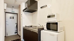 A compact kitchen with a microwave, stove, and oven. There is a door with a sign, a small sink, and a shoe rack by the door. - Nagomi by b hotel | Comfortable Studio Stay N62 (Hiroshima City)