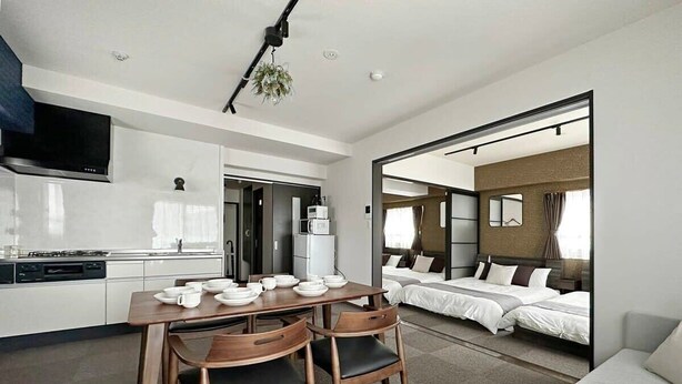Una habitación de hotel moderna con comedor, kitchenette y una cama grande con dos almohadas.