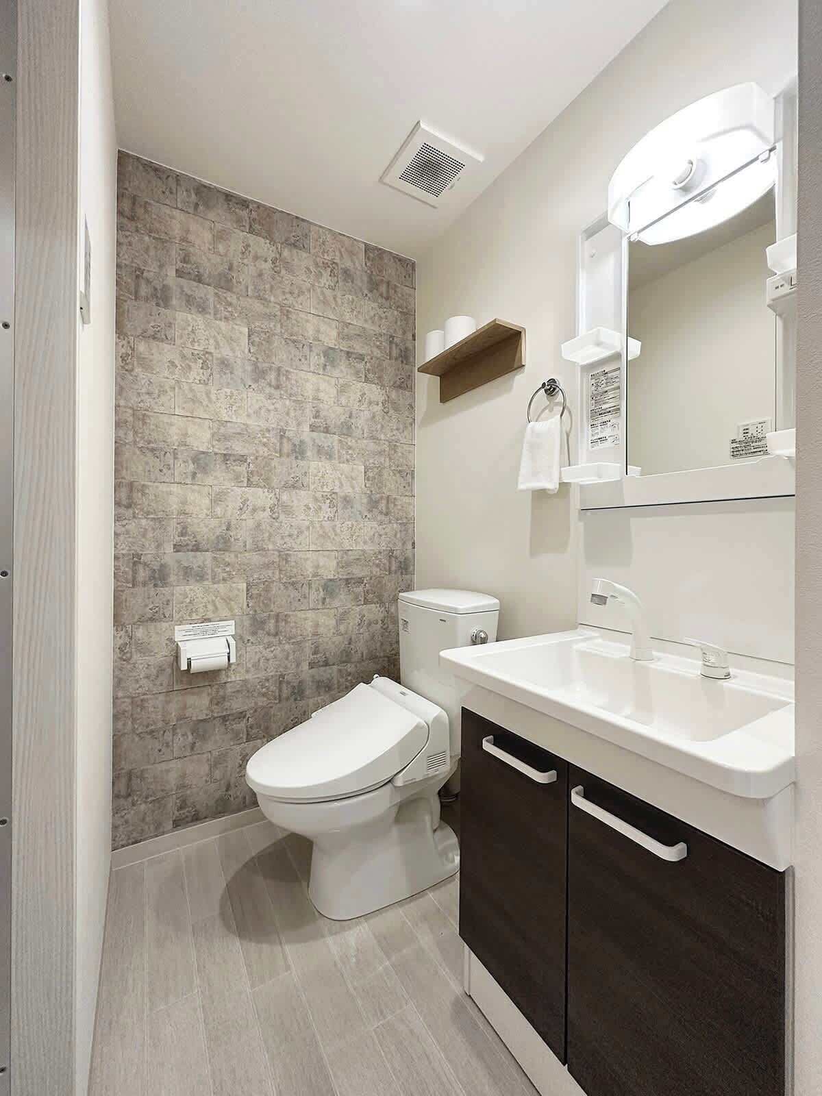 Un baño moderno con pared de piedra, inodoro, lavamanos con espejo y un perchero para toallas.