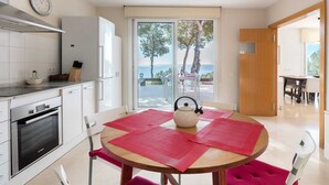 A modern kitchen with a Bosch oven, a dining area with a round table and red placemats, and a view of the sea through large glass doors. - Oliver House (Tarragona)
