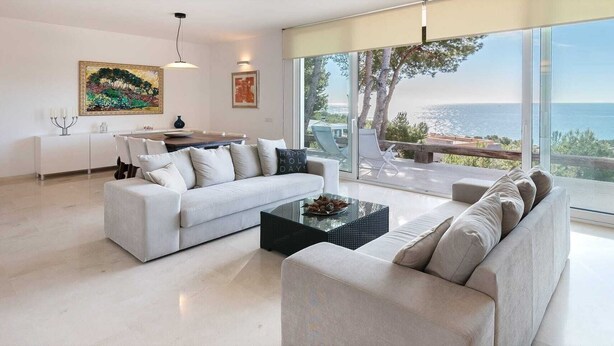 A modern living room with a white sofa, a black coffee table, and a large window offering a view of the sea. - Oliver House (Tarragona)