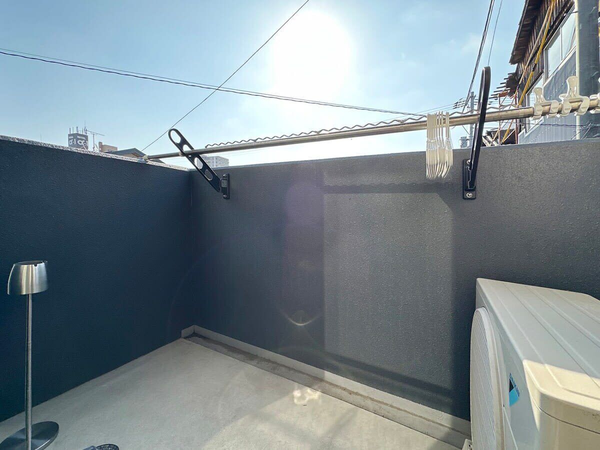 A small, enclosed balcony with a metal railing, a wall-mounted fan, and a metal floor lamp.