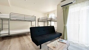 A dormitory room with bunk beds, a black sofa, a small table with a magazine, and a window with curtains. - 1Br Apt with Balcony for 4 Ppl in Onomichi (Onomichi)
