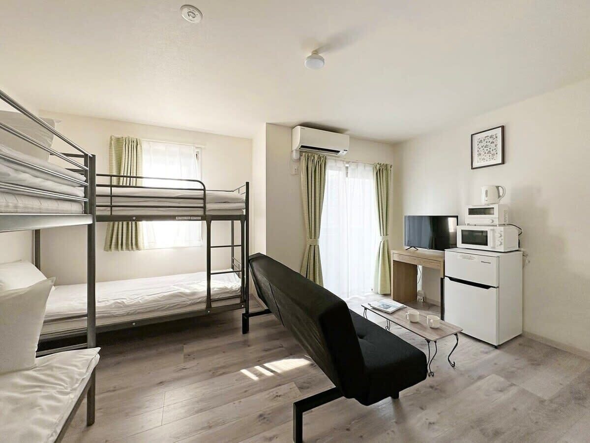 A dormitory room with bunk beds, a desk, a chair, a TV, a microwave, and an air conditioner.