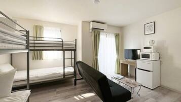 A dormitory room with bunk beds, a desk, a chair, a TV, a microwave, and an air conditioner.