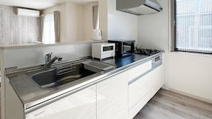 A modern kitchen with a stainless steel sink, a microwave, a stove, and a built-in oven. - Spacious 2BR Apartment very near the Station (Onomichi)