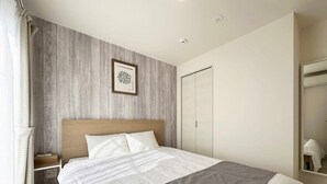 A modern hotel room with a wooden headboard, a large bed with a grey and white duvet, a bedside table, a wardrobe, and a mirror. - Spacious 2BR Apartment very near the Station (Onomichi)