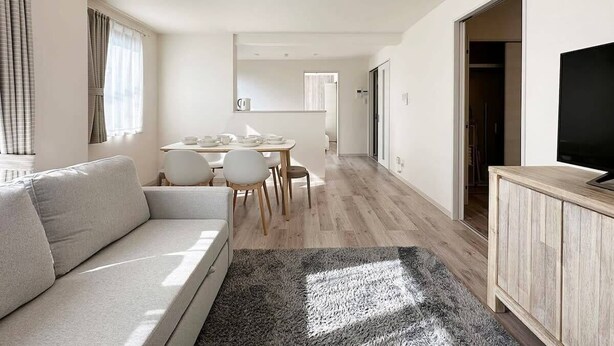 A modern living room with a sofa, dining table, chairs, and a TV on a wooden cabinet. - Spacious 2BR Apartment very near the Station (Onomichi)