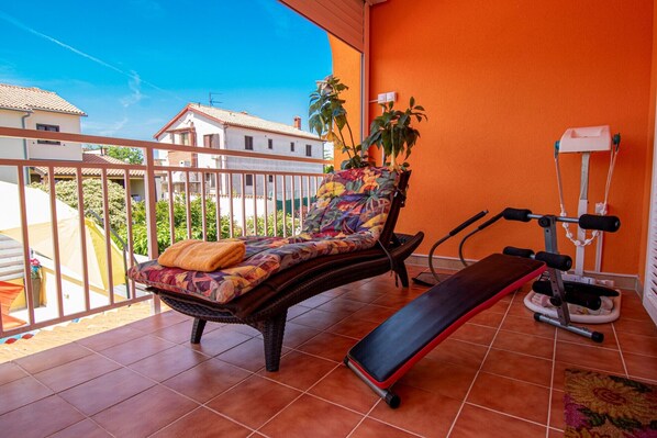 A balcony with a wicker chair, a bench, and a weightlifting machine.