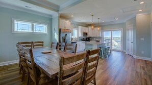 A spacious dining area with a wooden table and chairs, a kitchen with white cabinets, and a view through a glass door. - Flamingo Villa - Oceanfront B Luxury Home, Hot Tub, 6 bed 4.5 bath (North Topsail Beach)